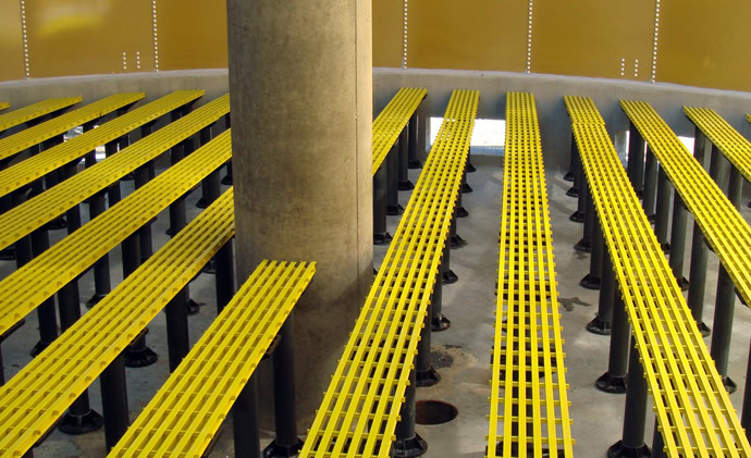 A symmetrical arrangement of yellow metal grates supported by black posts, arranged in parallel rows around a large central gray pillar.