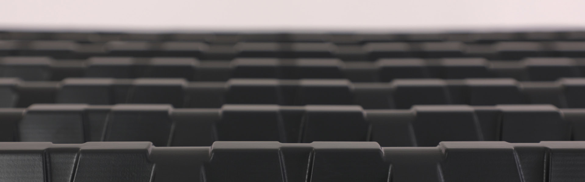 Close-up view of the top of a dark ribbed or grooved surface, resembling industrial or architectural materials, with repeated patterns extending out of focus in the background—like an AccuVent attic ventilation system.