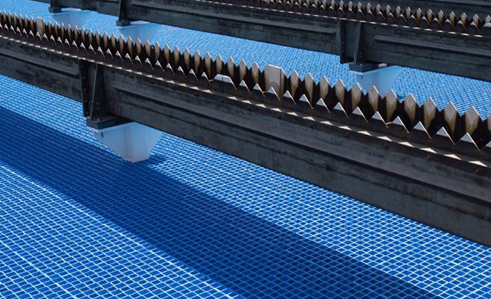 The IFR-6000 Series water treatment facility close-up shows blue tiled tanks with serrated metal skimmers or weirs used for filtering impurities from the water.