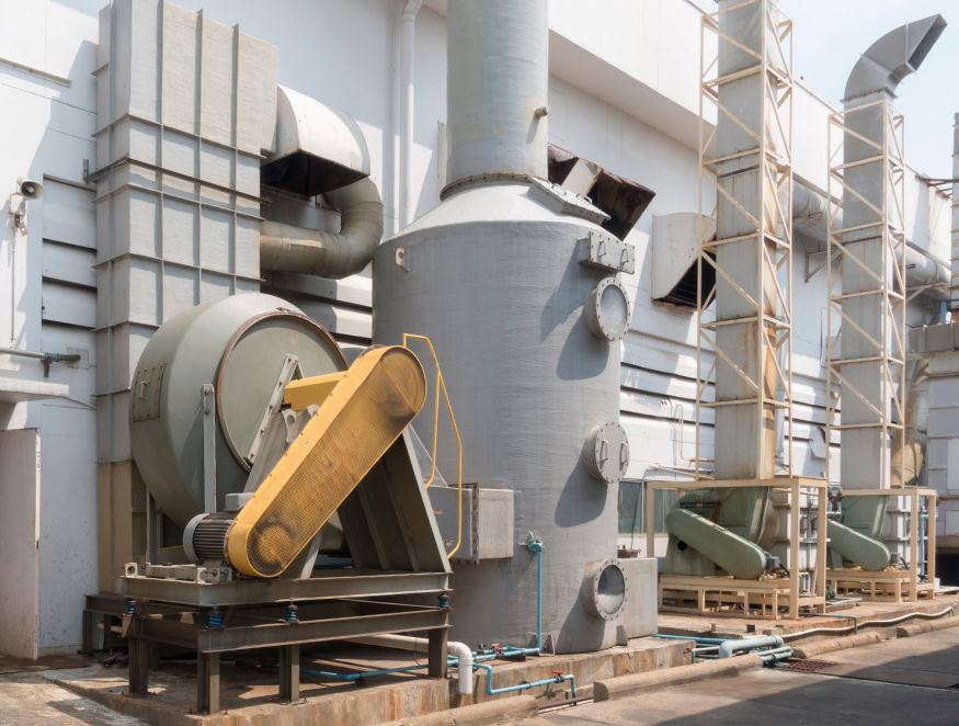 Instalación industrial con grandes sistemas de ventilación y depuración de gases. El equipo incluye depuradores cilíndricos, múltiples conductos y un gran ventilador industrial con motor incorporado.