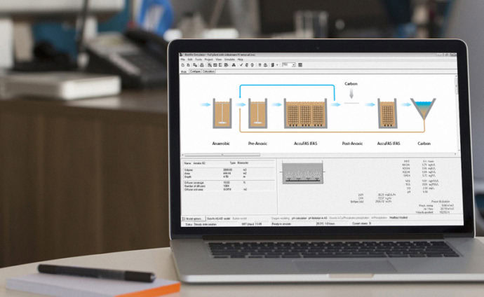 Un ordenador portátil sobre un escritorio muestra una interfaz de software con un diagrama del proceso de tratamiento de aguas residuales, etiquetado con etapas como anóxica, prenoxica, anóxica/tóxica (B) y carbono. .