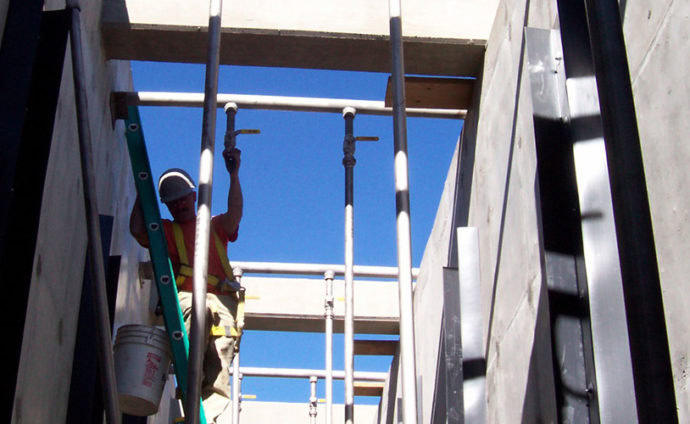 Un trabajador de la construcción con casco y equipo de seguridad está trabajando en un andamio entre dos estructuras de hormigón.