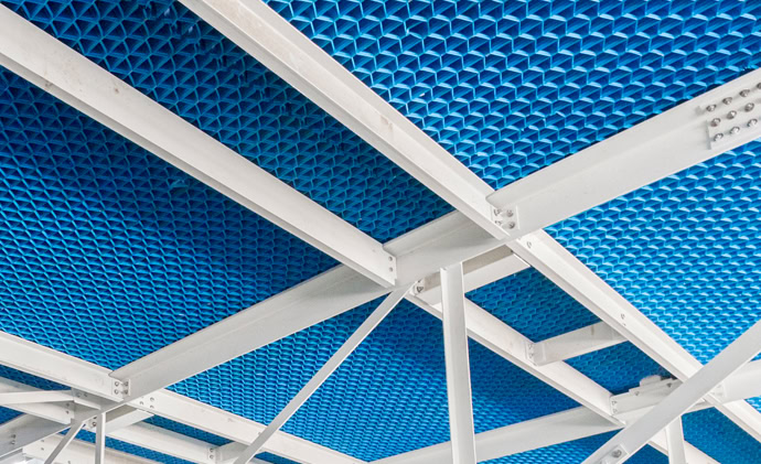 Close-up view of the underside of a metal structure with a blue perforated ceiling. The framework consists of white metal beams and supports creating a geometric pattern.