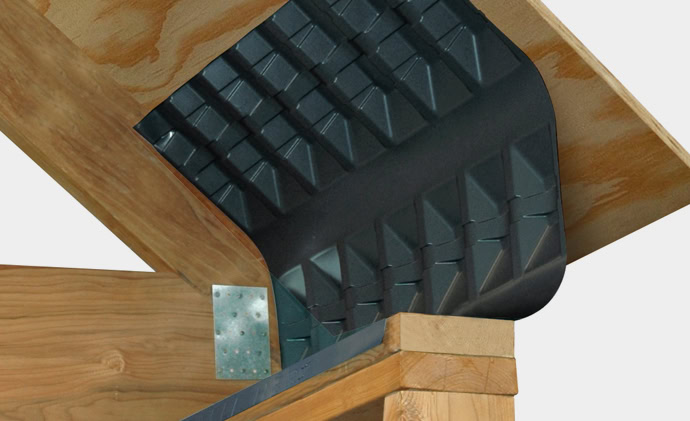 A close-up of a roofing installation showcases AccuBlock, with a black, grid-patterned underlayment being applied to a wooden roof structure. Metal brackets are visible, securing the wooden beams together and ensuring proper assembly for an efficient roof ventilation system.