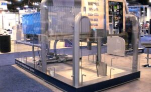 The display at the trade show showcases a new SedVac system, featuring a large piece of industrial machinery enclosed in a glass casing.