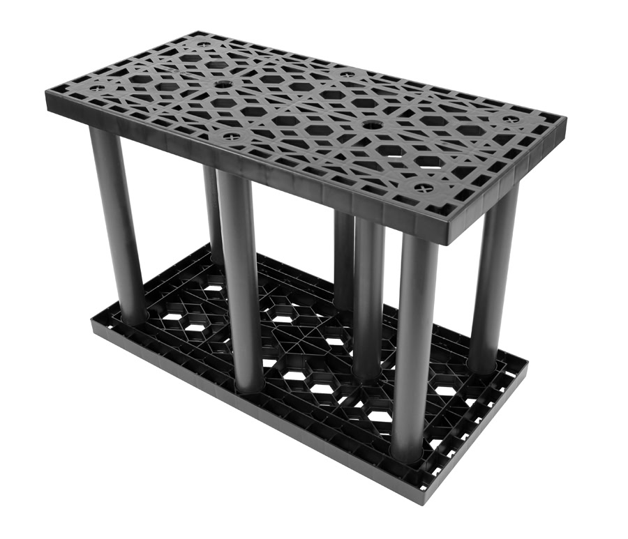 A black plastic storage rack featuring a perforated top and bottom shelf connected by six cylindrical columns. The geometric perforations provide ventilation, drainage, and aid in stormwater management.