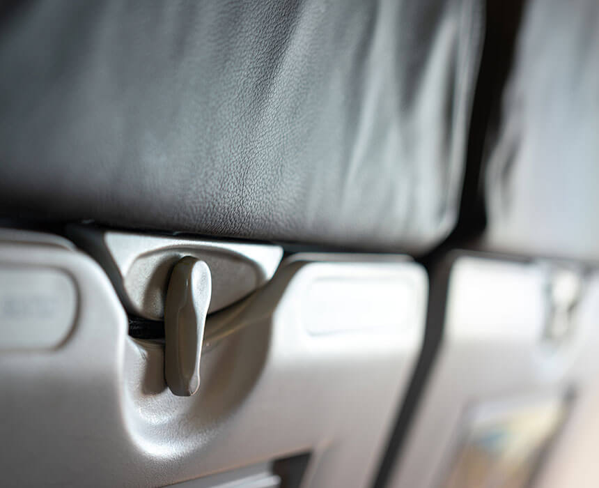 Close-up image of a tray lever on the back of an airplane seat, set against the leather upholstery of the seat back