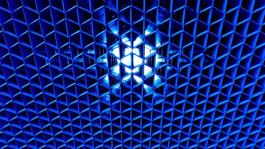 Un patrón geométrico de celdas hexagonales azules forma una estructura en forma de rejilla con una fuente de luz brillante y resplandeciente en el centro.