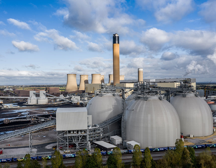 Un horizonte industrial con varias grandes instalaciones de almacenamiento en forma de cúpula en primer plano, con avanzadas chimeneas cilíndricas y torres de refrigeración al fondo.