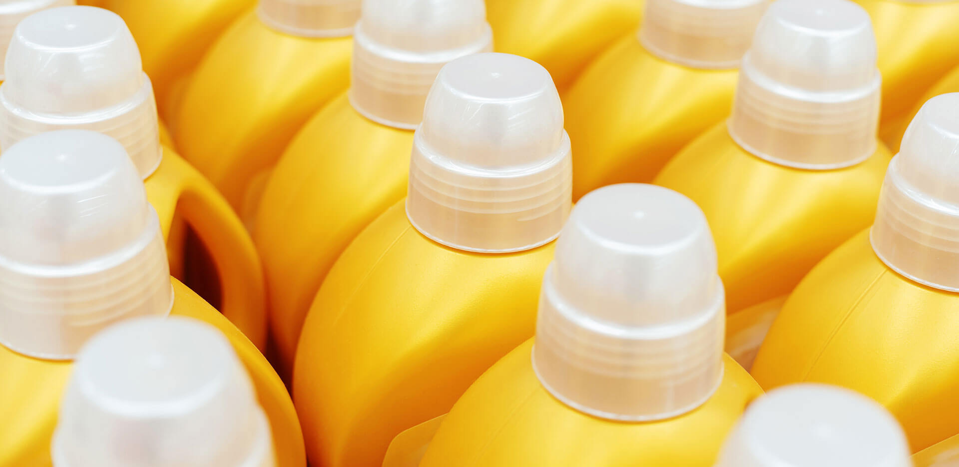 Rows of yellow plastic bottles with white caps, closely aligned, likely containing liquid detergent or a similar household product.