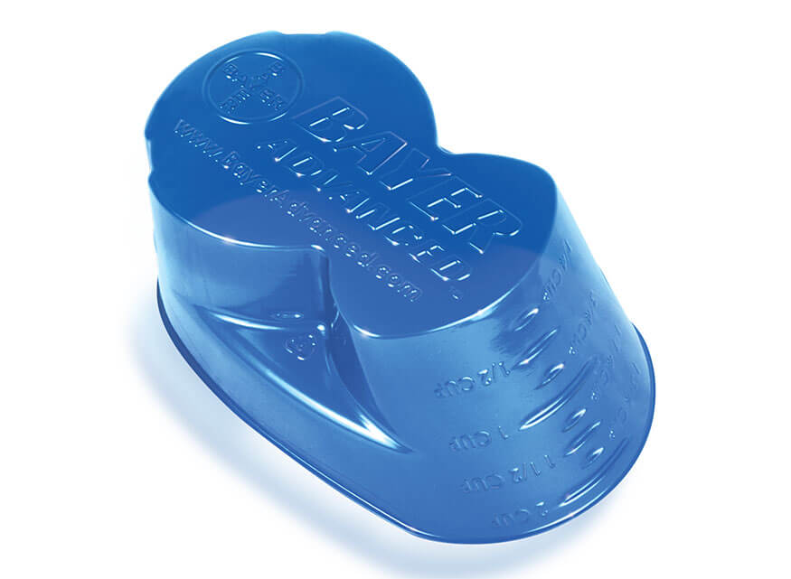 A blue plastic measuring cup with embossed text and measurement lines on it. The text reads "BAYER ADVANCED," along with other information related to dosage and branding.