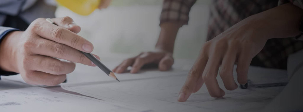 Close-up of two people working on architectural blueprints. One person is holding a pencil and making notes, while the other is pointing at the plans.