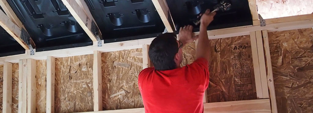 A person in a red shirt uses a tool to install Accuvent into the wooden framework of a roof.