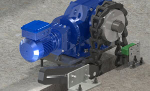 A blue motorized mechanical device, known as a drive unit assembly, is mounted on a concrete surface with bolts. It connects to a chain and sprocket system adjacent to a metal frame.