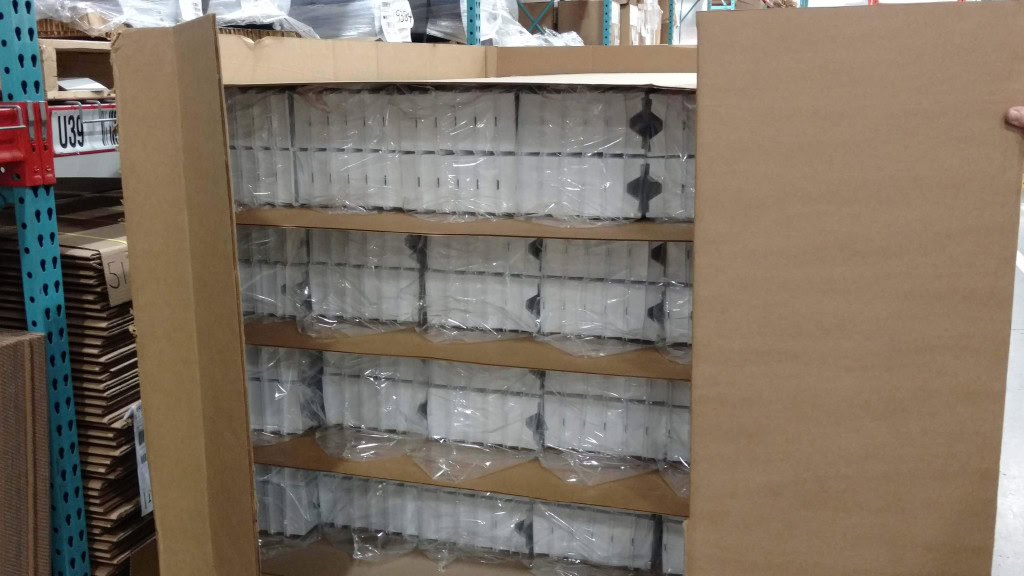 A large cardboard package contains several shelves of neatly organized, individually wrapped medical bottles. The package is partially open, exposing the top of the shelves and rows of healthcare supplies inside.