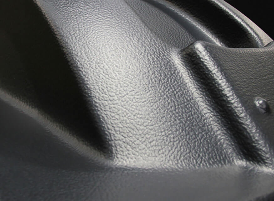 Close-up image of a surface with a textured, matte finish. The surface features curved and angular ridges. The lighting accentuates the texture, creating subtle shadows and highlights.