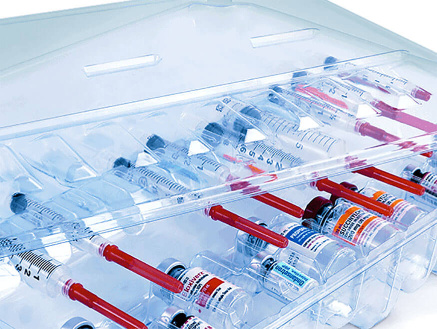 A clear plastic container, holds multiple syringes and vials arranged neatly in rows. The syringes have red plungers, and the vials are labeled with various colored tags.