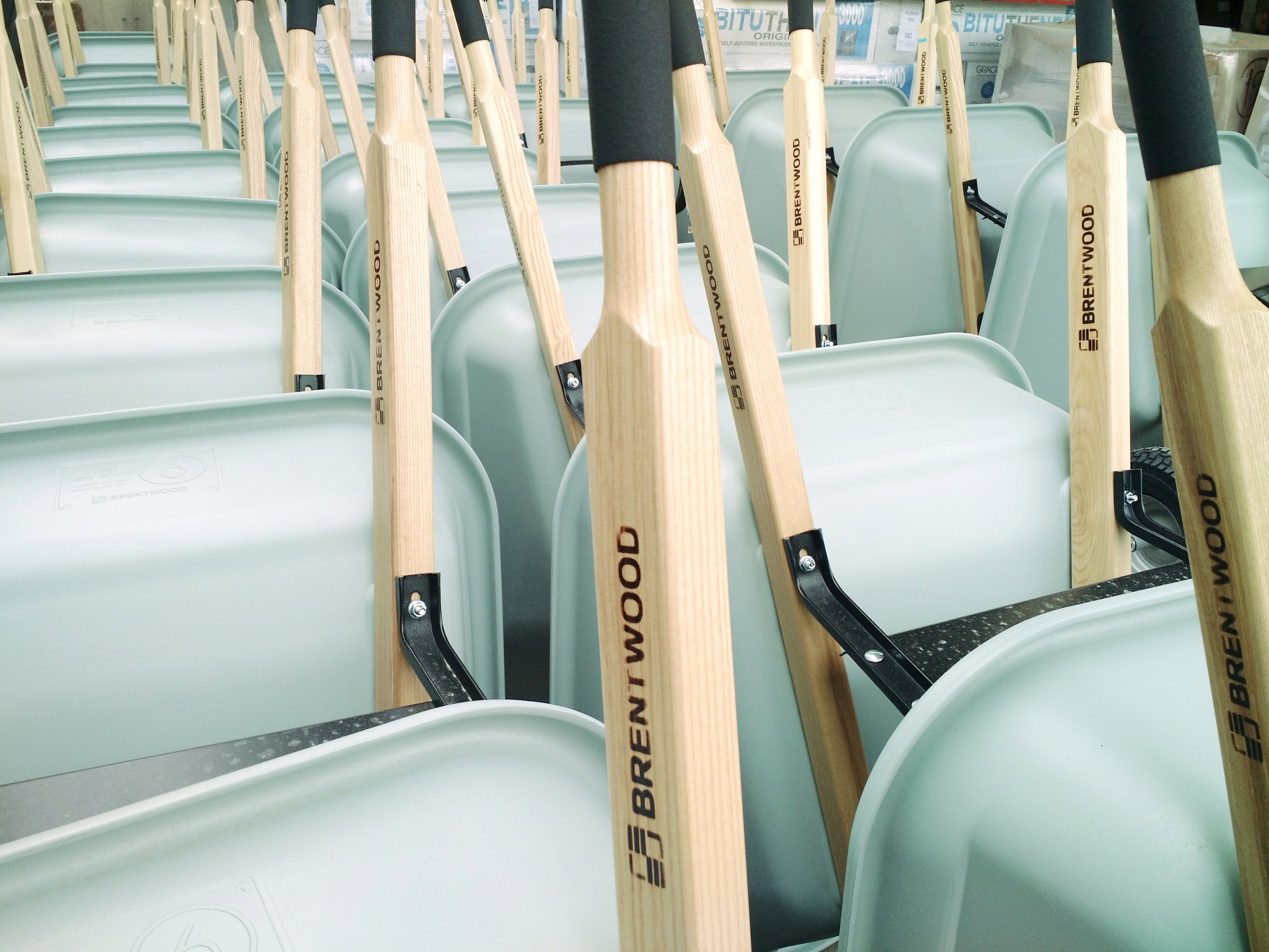 Rows of Brentwood Wheelbarrows standing vertically. They're all a teal color with wooden handles and a soft grip.