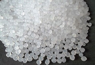 A close-up image of a heap of small, translucent white plastic pellets spread on a dark surface.