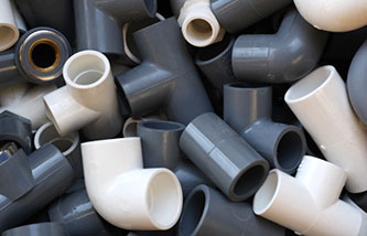 A pile of assorted PVC pipe fittings in various shapes and sizes, including elbows, tees, and straight connectors. The fittings are primarily grey and white in color