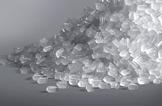 A large pile of transparent plastic pellets made from PVDF is scattered on a flat surface against a plain background.