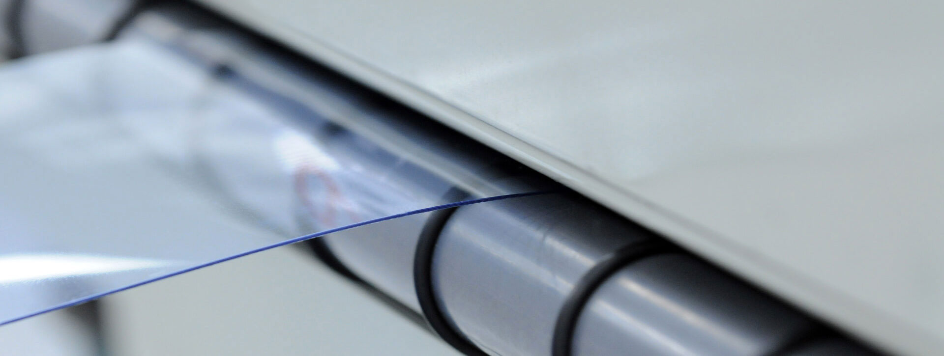 A thin, plastic material being fed through a set of rollers in a machine.