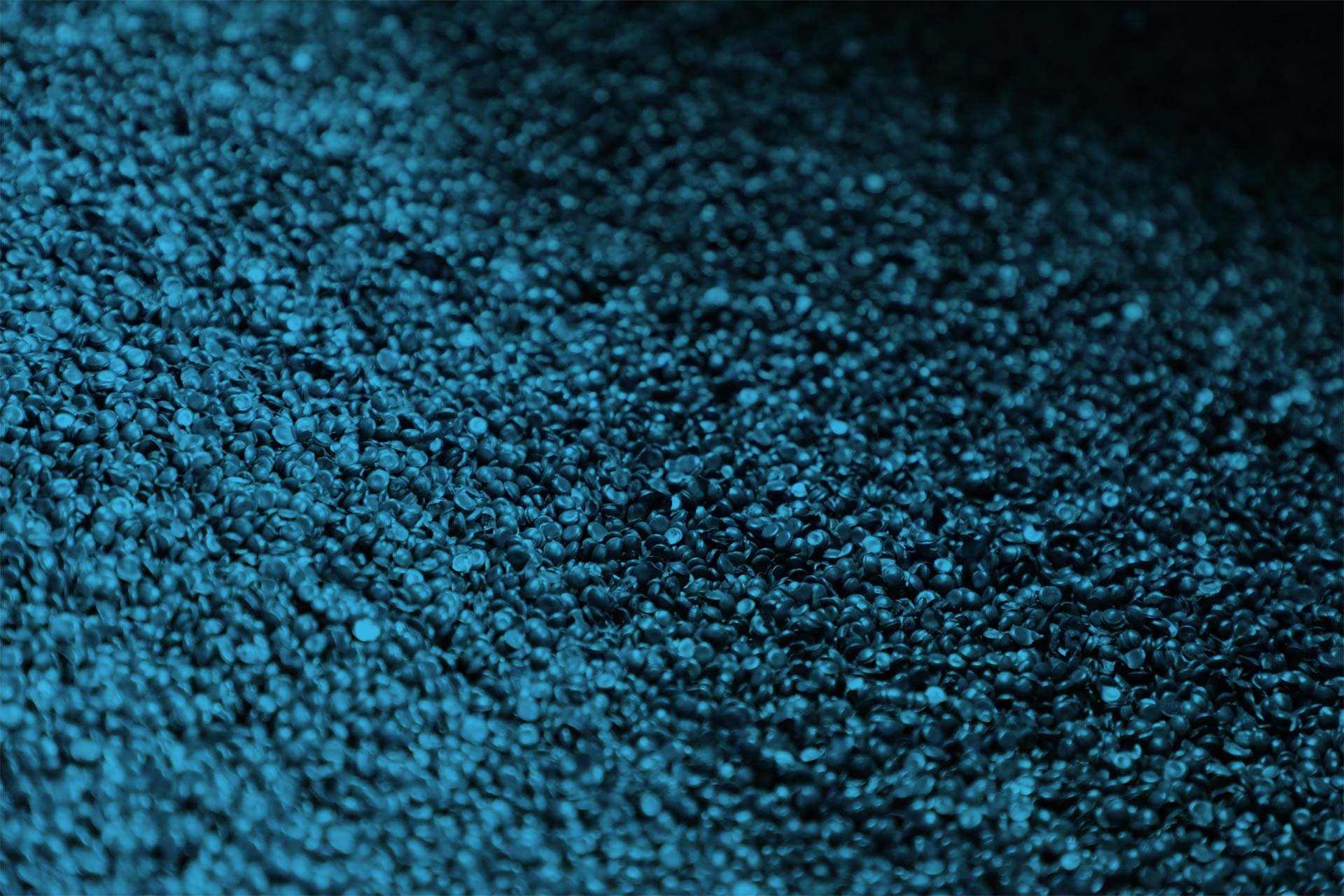 Close-up view of thousands of small, dark blue granules or pellets densely packed together, creating a textured and somewhat metallic surface.