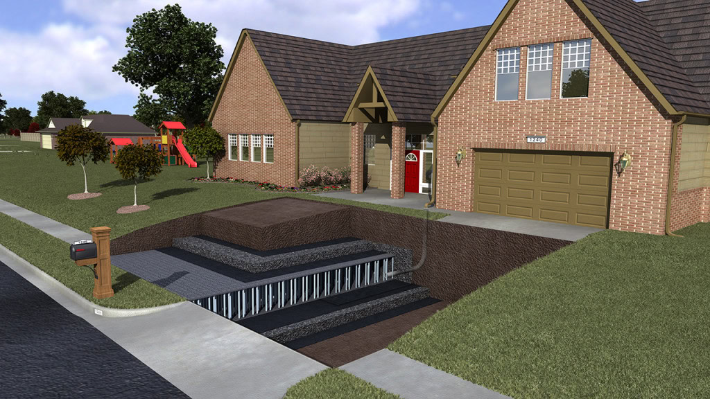 A suburban brick house with a gabled roof features an underground stormwater management structure beneath the driveway. The structure has tiered levels, railings, and stairs. The front yard boasts green grass and trees, with a colorful playground visible in the background.