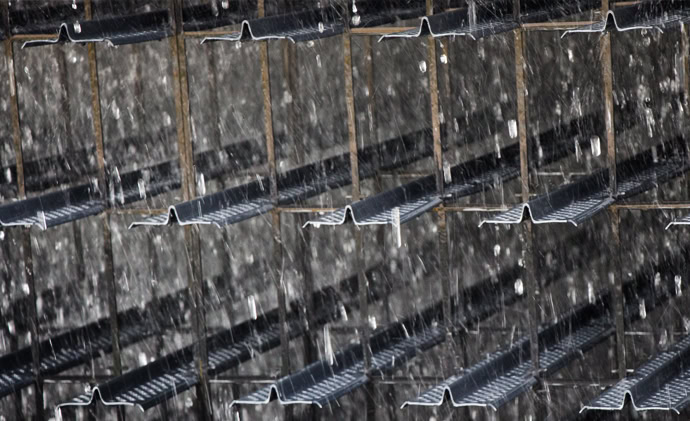 Close-up of a cascading waterfall flowing over multiple tiers of splash fills, creating a repetitive and rhythmic pattern. The water splashes and sparkles as it moves.