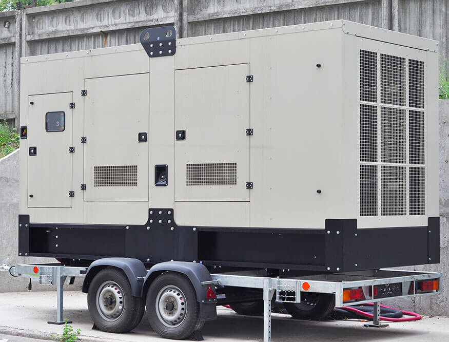 A large, beige industrial generator mounted on a black and silver trailer is parked outdoors. This power unit boasts ventilation grilles and access panels, ensuring efficient operation.