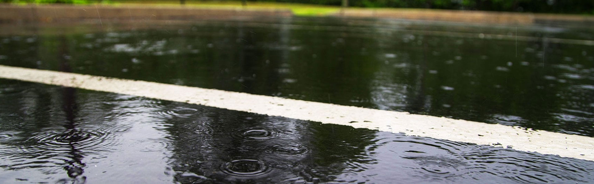 Primer plano de gotas de lluvia que crean ondulaciones en una superficie exterior mojada, probablemente parte de una carretera o zona pavimentada.