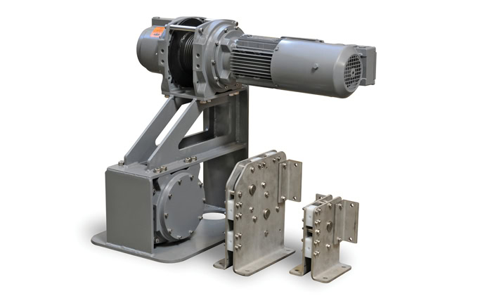 A metal industrial machine with a motorized mechanism mounted on a sturdy base, adjacent to two smaller metal components with bolts. The machine and components are gray.