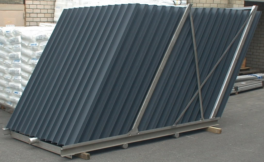 A stack of corrugated metal sheets is arranged in an angled, upright position on a wooden pallet. The sheets are supported by a metal frame. This is the TUBdek.