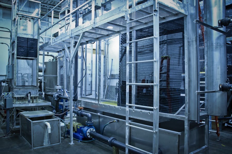 A complex arrangement of industrial equipment and machinery composed of metal framework, pipes, and pumps is set up in a factory environment.