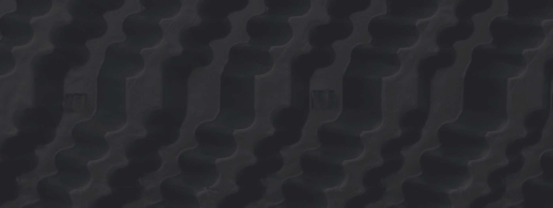 Close-up of a black textured surface with a repeating, wavy pattern that creates a series of vertical ridges and indentations.