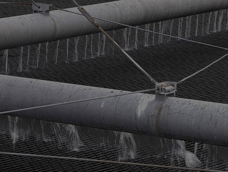 Close-up of industrial pipes arranged horizontally, with water flowing out in multiple thin streams. The background consists of a grid-like structure.