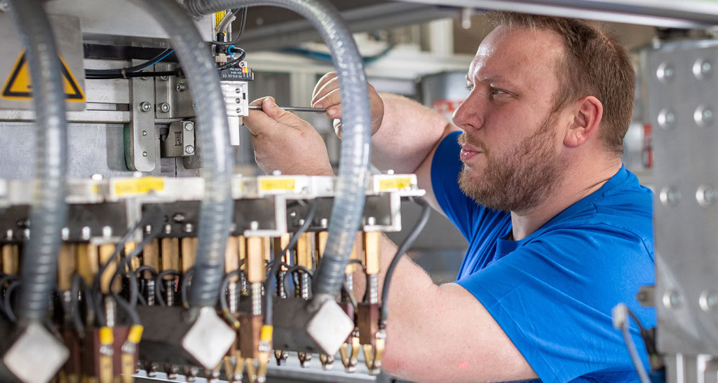 Un hombre con camisa azul se concentra en la reparación o instalación de un componente en una compleja máquina industrial en Wettringen, Alemania.