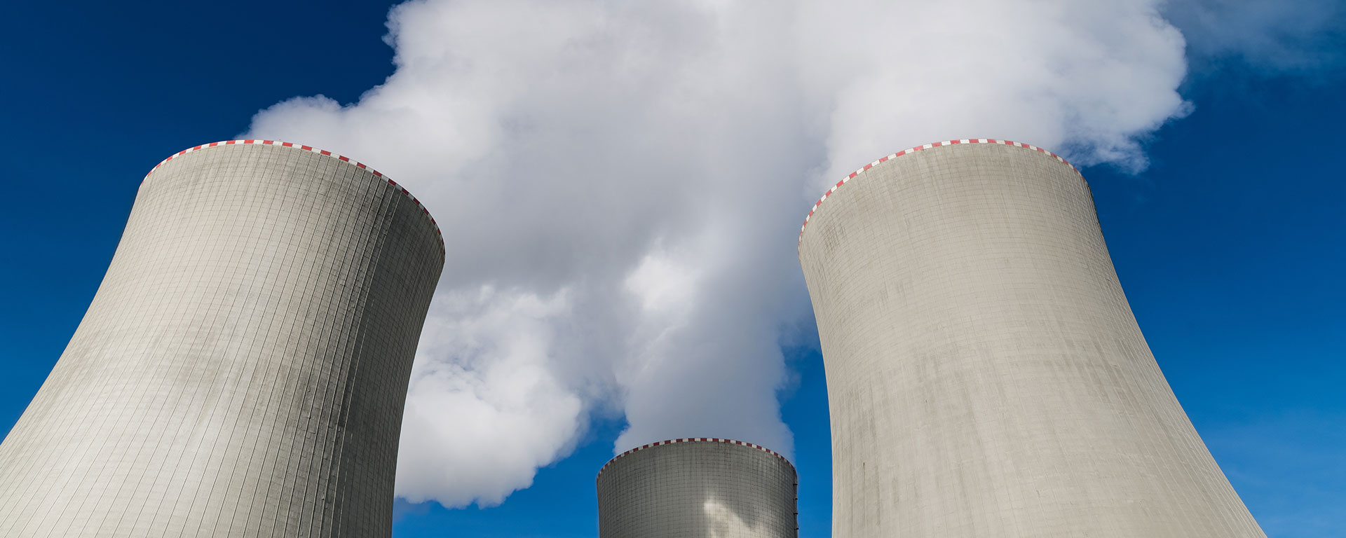 A close-up view of three power plant cooling towers emitting white steam against a clear blue sky.