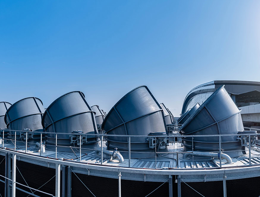 A row of large, advanced industrial cooling towers with cylindrical ducts is positioned on the rooftop of a building.