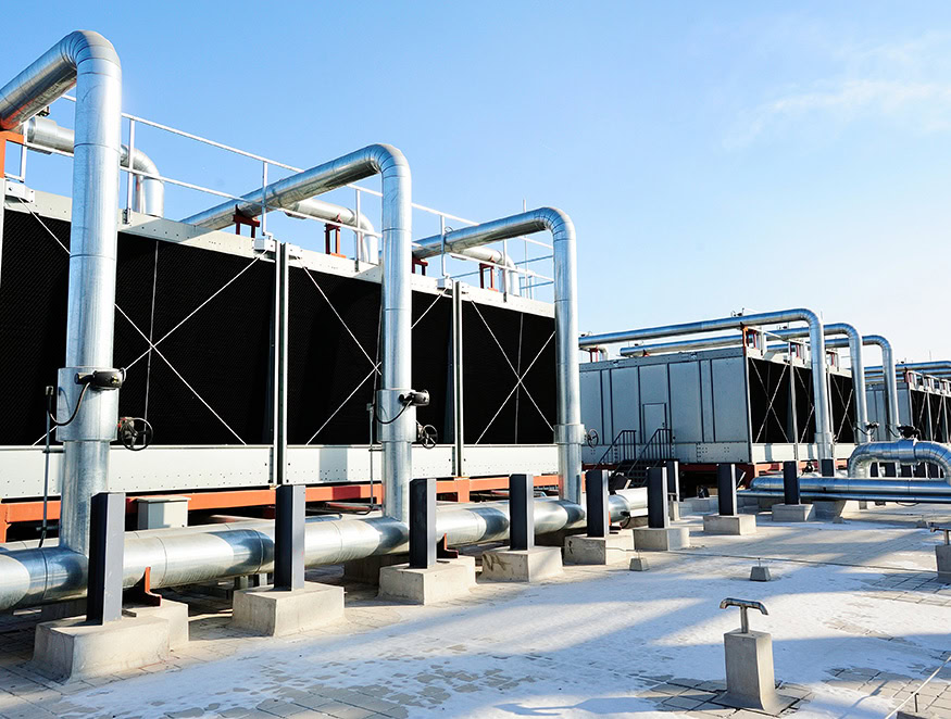 Industrial cooling system with large metal pipes and heat exchangers set against a blue sky.