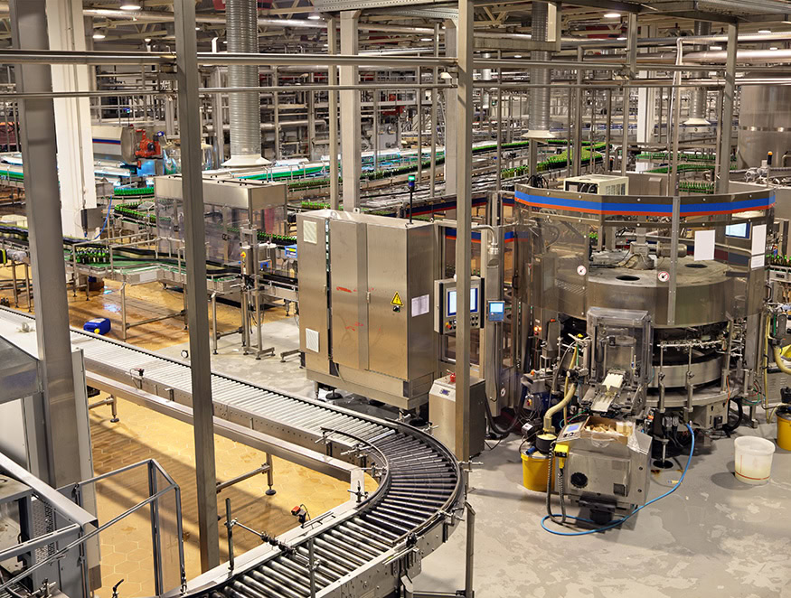 A large, modern food processing plant with various industrial machinery and conveyor belts transporting green bottles.