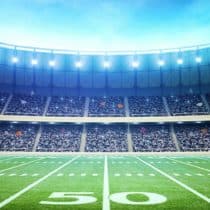 A vibrant football stadium packed with spectators. The image is taken from ground level, facing the 50-yard line on a well-manicured field.