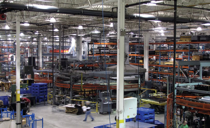 A large industrial warehouse with shelves stocked with various materials and equipment. The space features high ceilings with exposed beams and bright lighting.