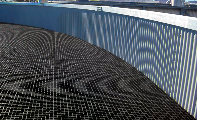 The image shows an industrial structure with a metal floor composed of a grid pattern and a corrugated metal wall curving around the perimeter. The structure showcases the accugrid trickling filter.