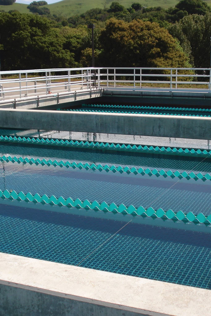 Outdoor water treatment facility with multiple rectangular, open tanks filled with potable water, separated by blue baffles.