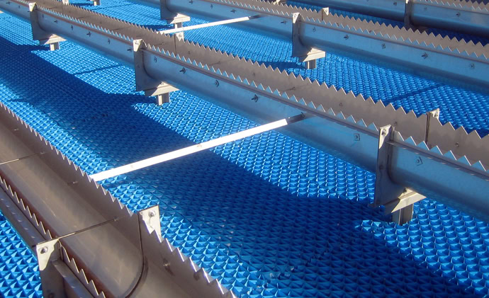 A close-up view of a metal structure with a blue, textured platform. Jagged metal beams and support brackets provide an industrial look, while a white rod runs horizontally across the image.