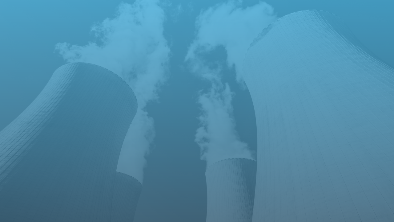 Image shows four large cooling towers emitting white plumes of steam against a clear sky.