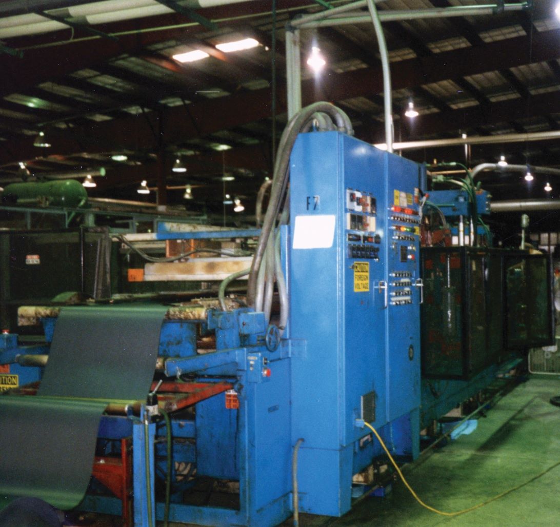 A large industrial machine with blue panels and various control switches and buttons stands in a factory with dim lighting, reminiscent of historical events in the evolution of manufacturing.