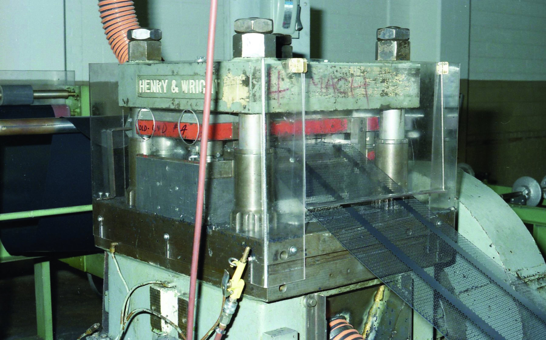 An industrial machine labeled "Henry & Wright" with various pipes and cables attached, showcasing a blend of engineering prowess and history. The machine features a transparent protective cover and processes a dark material through its rollers.