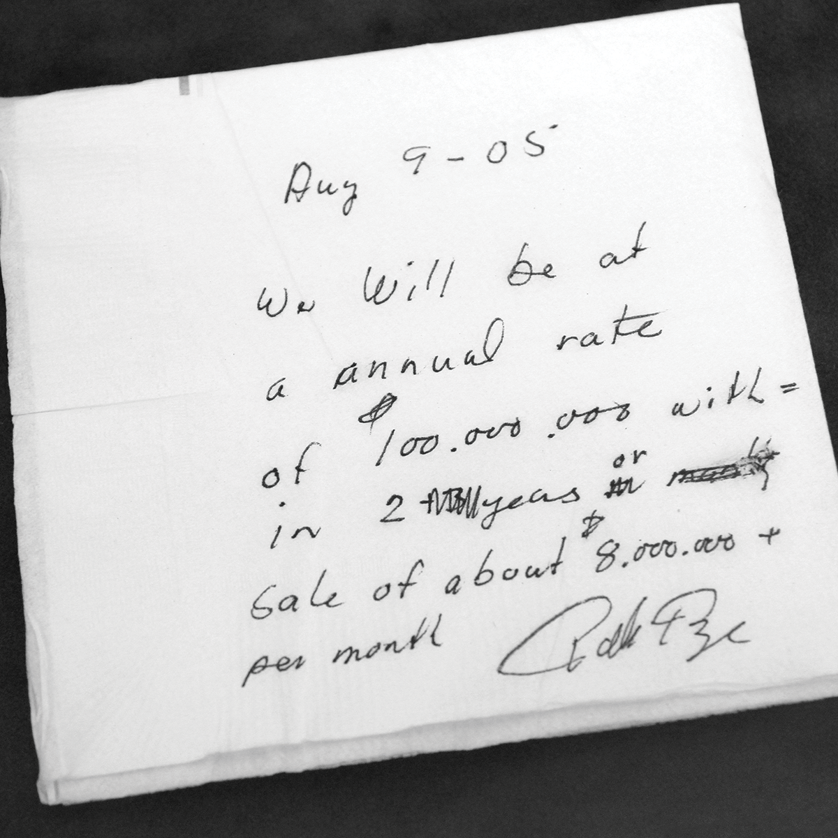 A handwritten note on a napkin, dated Aug 9 '05, outlines historical financial projections. The text reads: "We will be at an annual rate of 100,000.000 within 2-3 years or sale of about 8,000.000+ per month." It is signed at the bottom.